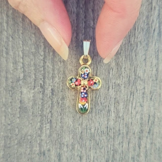 Pendentif croix chrétienne dorée ornée de motifs colorés, tenu entre deux doigts