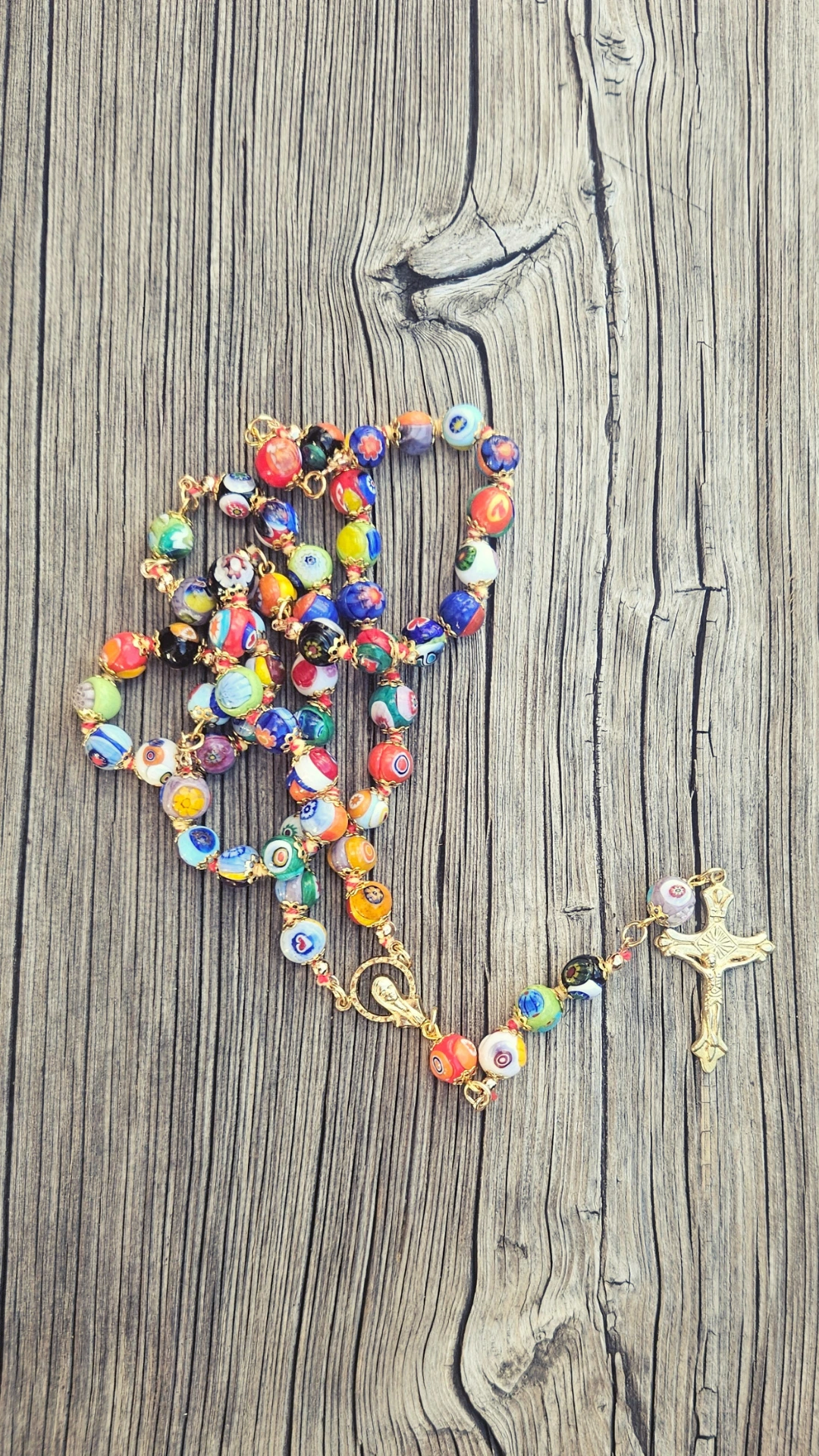Chapelet en verre de Murano aux perles multicolores ornées de murrines, avec un crucifix doré, posé sur du bois